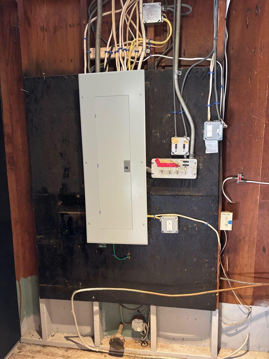 Closed gray electrical panel and surrounding conduits on a timber wall, in a photo shared by Bright.